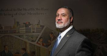 Fordham Law grad Mark Torres, general counsel for the Teamsters Union Local 810, stands in front of a New Deal-era, pro-union mural created by Auriel Bessemer. The text on the mural reads in part, "Dedicated to the Health, Welfare and Well-being of Our Members."
