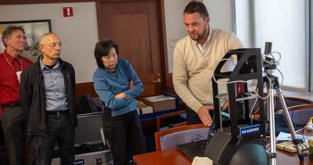 A man demonstrates a scanner to three members of the Fordham Libraries staff