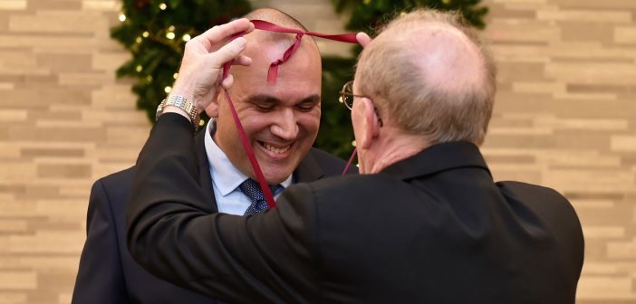 An awardee smiles and looks down as Father McShane slings a medal around his neck.
