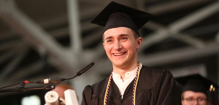A boy wearing a black graduation gown smiles