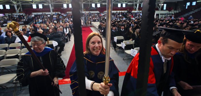 A woman wearing a faculty graduation gown holds a pole