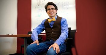 A man wearing a bow tie smiles in a classrooms setting.