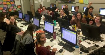 Students sitting in front of computers, wearing headsets and smiling at the camera