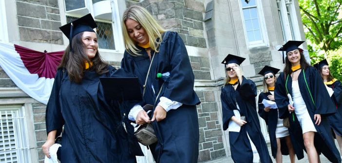 Two women wearing black graduation gowns smile while they walk.