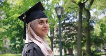 Naimal Chisti, wearing a hijab and a black graduation cap, smiles into the distance.