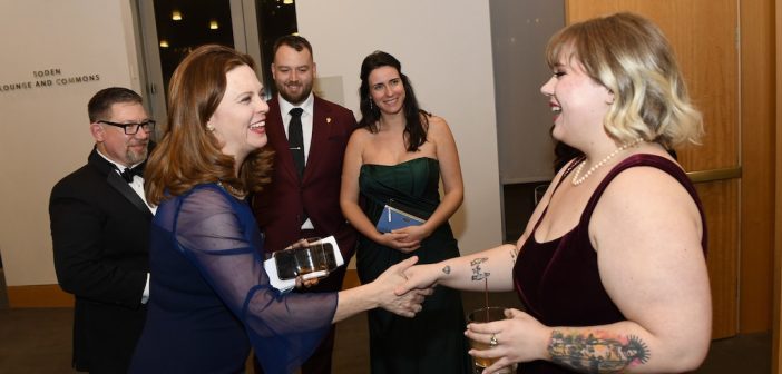 Tania Tetlow joyously shakes hands with someone while three onlookers smile.