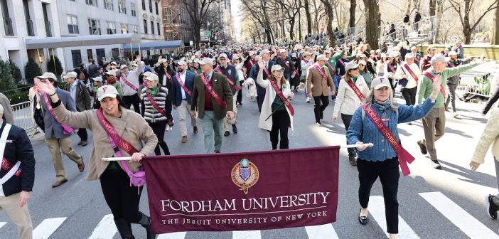 A group of parade participants hold a Fordham banner and smile and wave at the crowd.