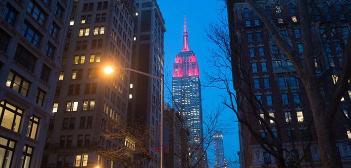 The Empire State Building lit up maroon. NYC buildings in the forefront.